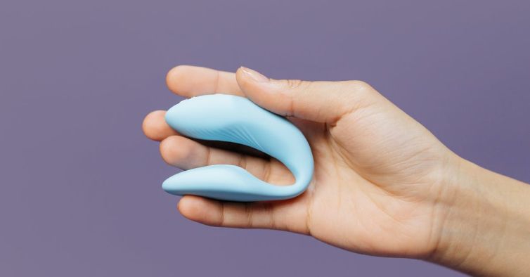 A hand holding a small blue vibrator against a purple background, symbolizing intimacy.