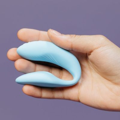 A hand holding a small blue vibrator against a purple background, symbolizing intimacy.